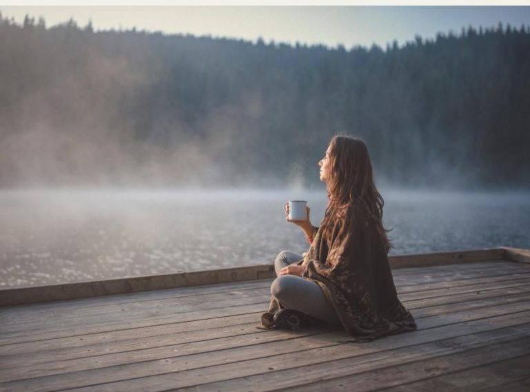 Woman in Los Angeles looking out at water and trees, drinking tea, relaxed. Woman is relaxed after internal family systems therapy in Los Angeles.