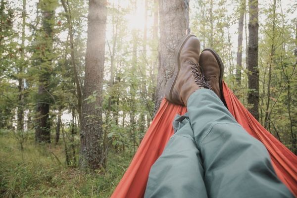 A peaceful scene showing a man’s worn hiking shoes poking out from a hammock, gently swaying between trees at a quiet Los Angeles campsite.