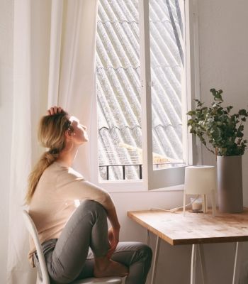 Woman gazing out the window in her Los Angeles apartment, reflecting on growth through somatic therapy for people-pleasing