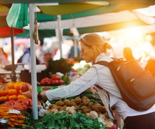 Woman in los angeles at farmers market, taking care of herself after holistic therapy. Woman has blonde hair, jean jacket, and backpack