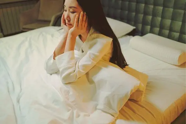 Woman sitting on bed with hands on face, looking emotionally shut down — Los Angeles anxiety and trauma therapy