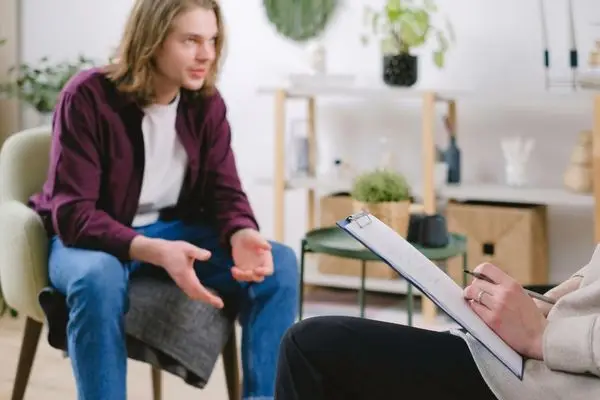 A somatic therapist in Los Angeles takes notes while listening to a client during a face-to-face therapy session.