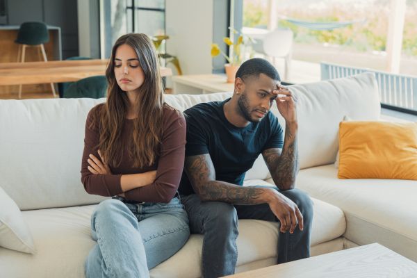 Couple sitting apart on a couch and looking away from each other, showing the emotional distance that can grow in a codependent relationship