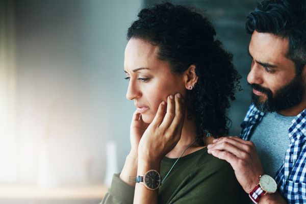 Man gently comforting a woman by a window with his hands on her shoulders, showing support in an interdependent relationship