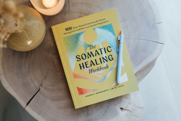 Lifestyle image of The Somatic Healing Workbook by Cheryl Groskopf, LMFT, LPCC. The workbook teaches readers how fight, flight, freeze, and fawn responses show up in everyday life and includes somatic exercises for stress and nervous system regulation.